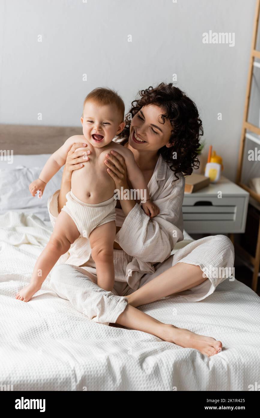 donna felice con capelli ricci sorridendo mentre tiene in braccio bambino eccitato, immagine di scorta Foto Stock