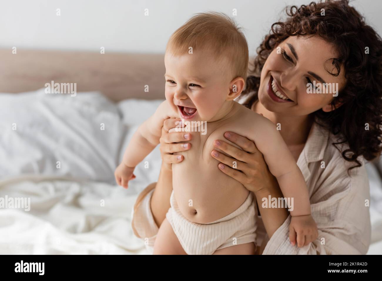 donna allegra con capelli ricci sorridendo mentre tiene in braccio bambino eccitato, immagine di scorta Foto Stock