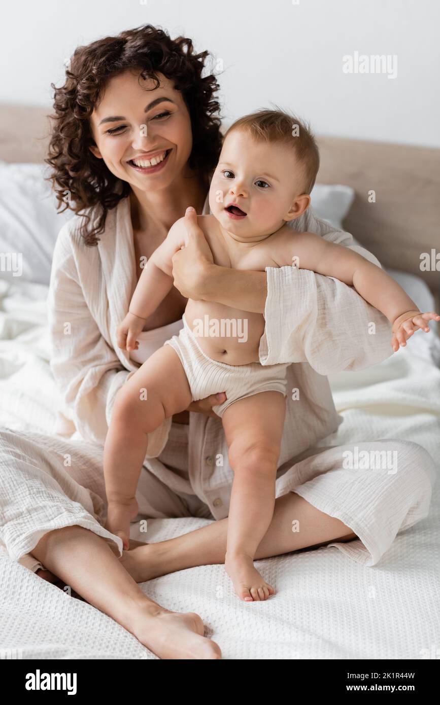 donna allegra in loungewear tenendo in braccio bambino stupito figlia con bocca aperta, immagine di scorta Foto Stock