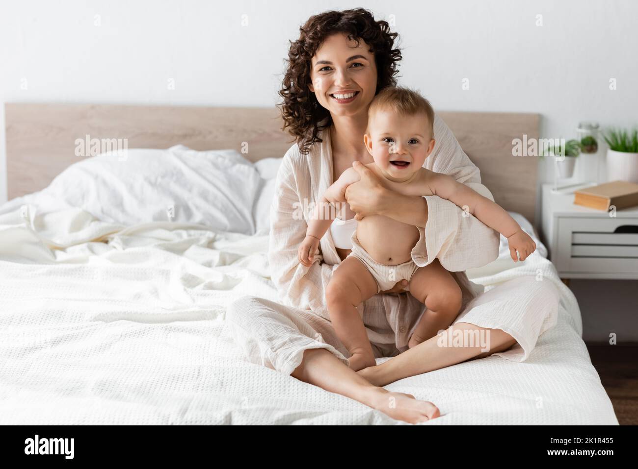donna gioiosa in loungewear tenendo in braccio sorpresi bambino figlia con bocca aperta, immagine di scorta Foto Stock