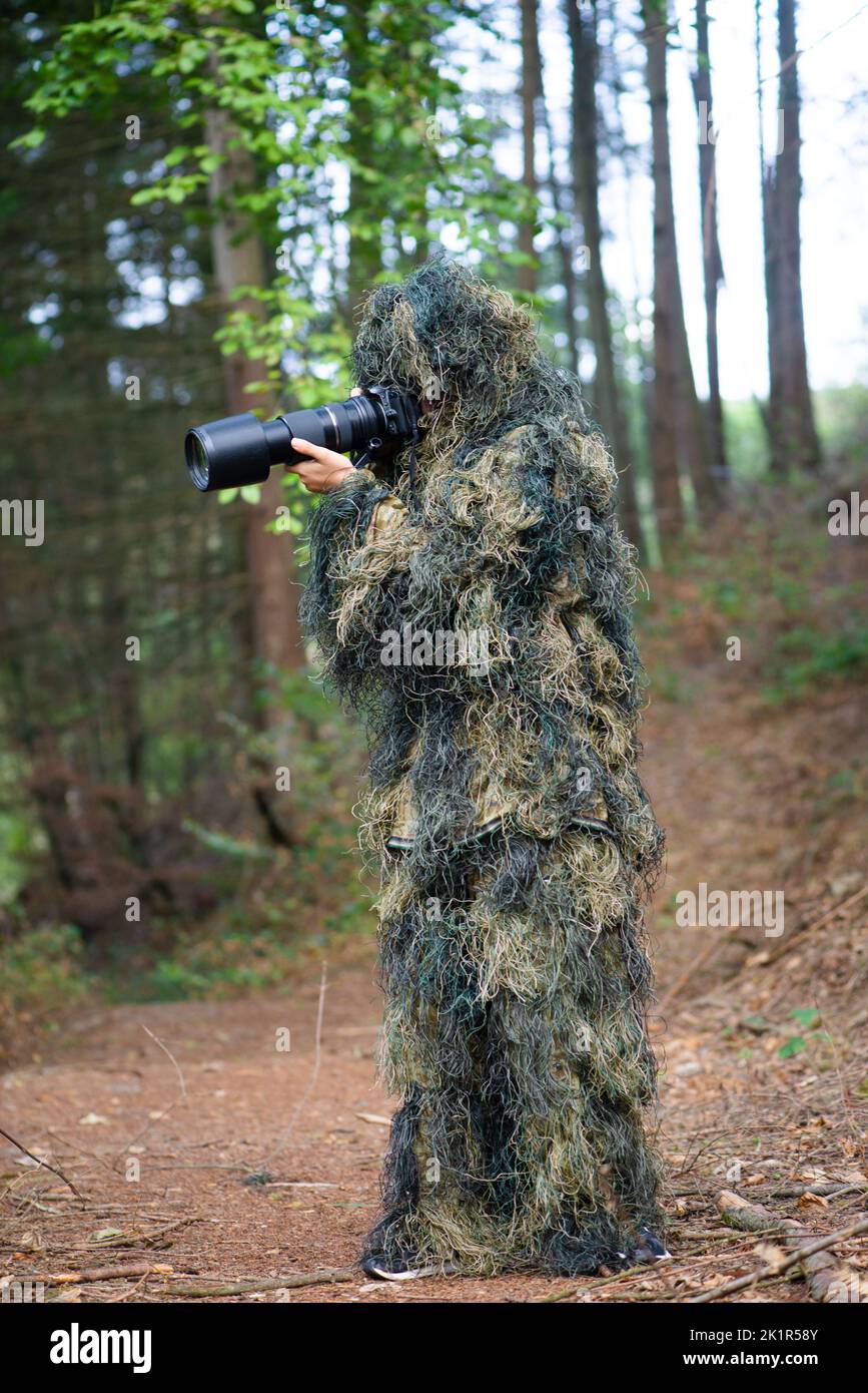 Fotografo che indossa abiti camouflage nella foresta, fotografia di animali selvatici con una macchina fotografica e teleobiettivo Foto Stock