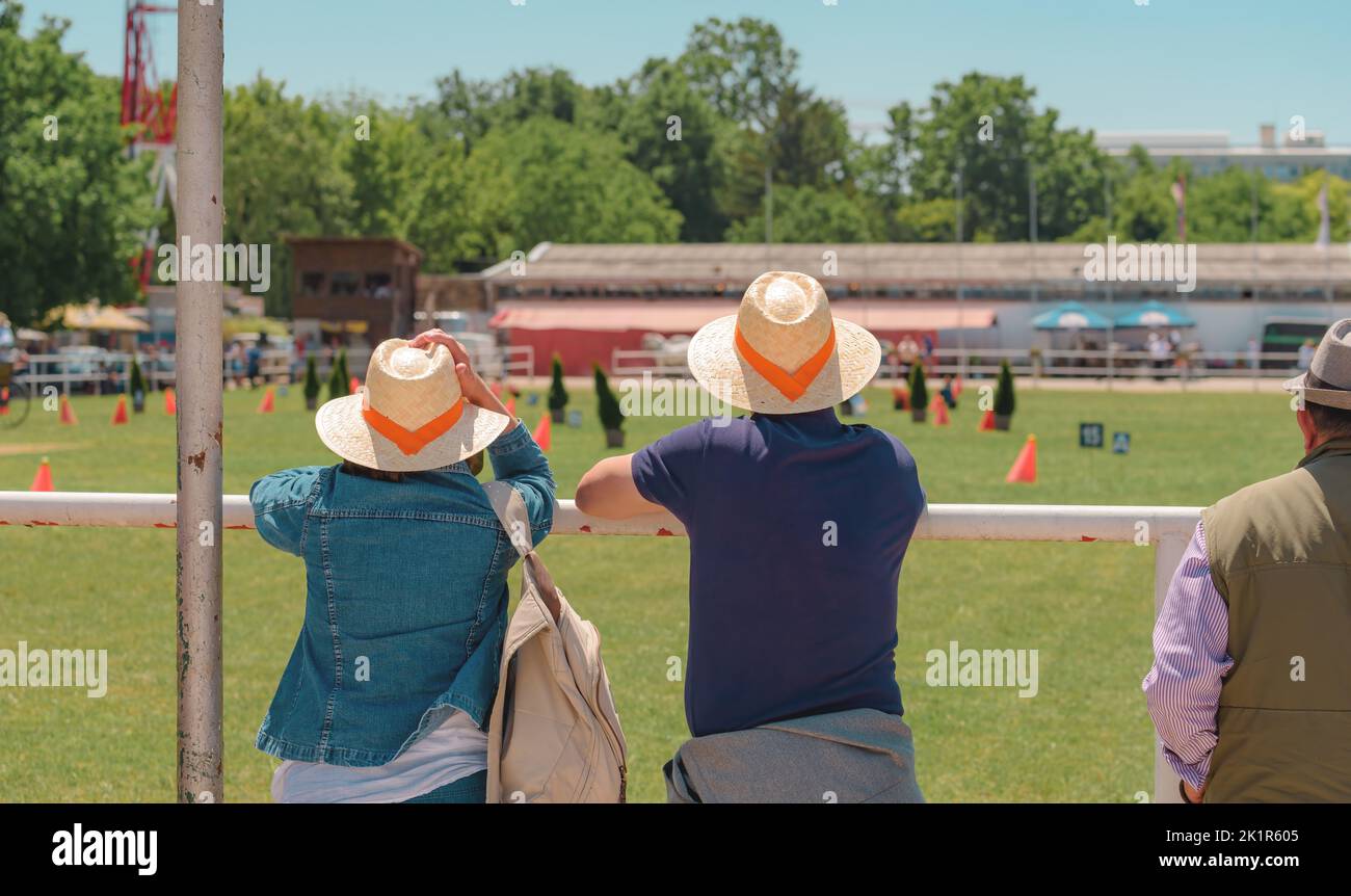 Gruppo di persone informali irriconoscibili che indossano cappelli di paglia con una band arancione all'evento pubblico equestre dal vivo il giorno estivo soleggiato, focus selettivo Foto Stock