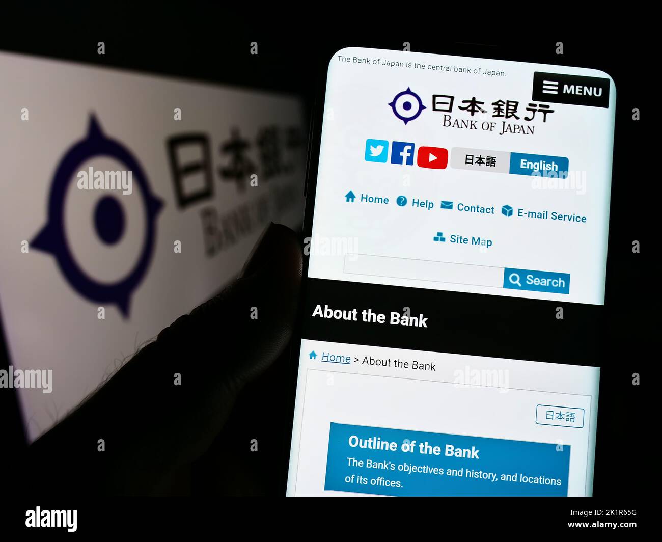 Persona che tiene uno smartphone con il sito Web dell'istituto finanziario Bank of Japan (BOJ) sullo schermo davanti al logo. Messa a fuoco al centro del display del telefono. Foto Stock