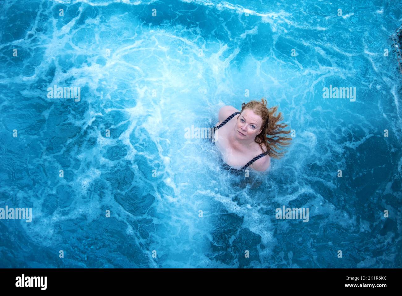Bella donna matura naturale sexy rosso testa in costume da bagno in acqua turchese turchese vorticoso blu nella piscina benessere Spa, spazio copia Foto Stock