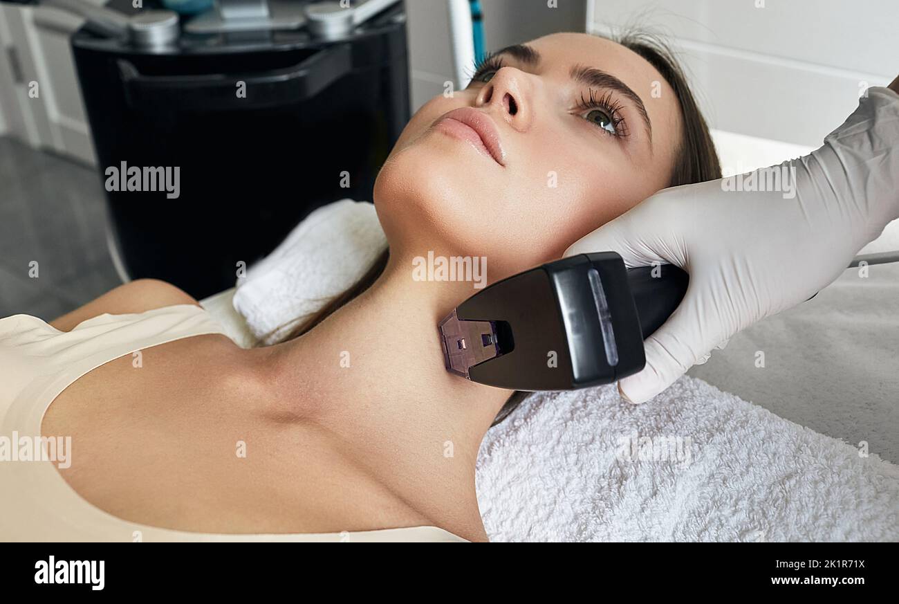 Bella donna che ottiene rf-lifting per il suo collo e corpo. Procedura di sollevamento RF presso il salone di bellezza con estetista Foto Stock