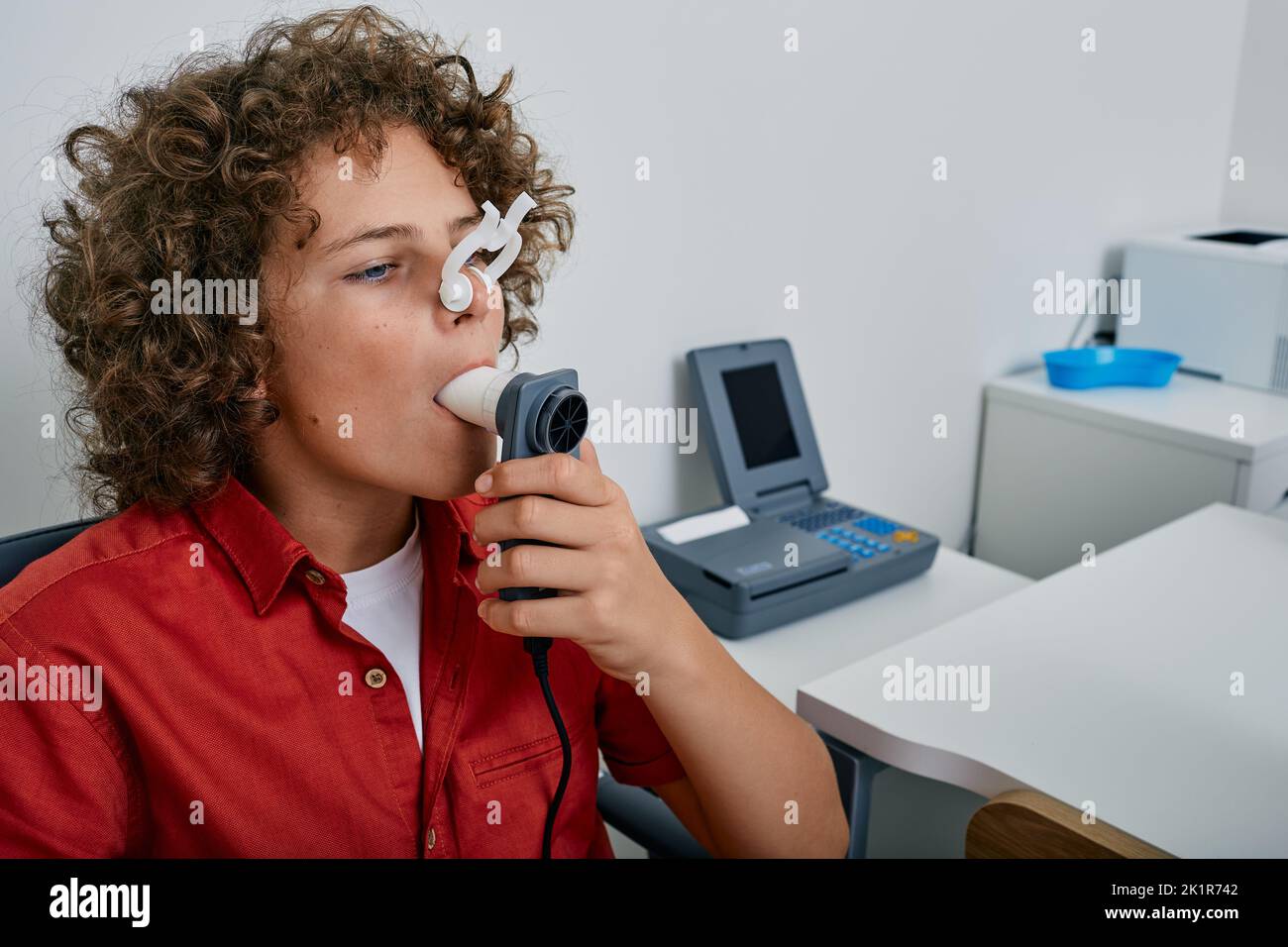 Curly ragazzo che esegue test di funzionalità polmonare e spirometria utilizzando spirometro in clinica medica. Spirometria dei polmoni del bambino Foto Stock