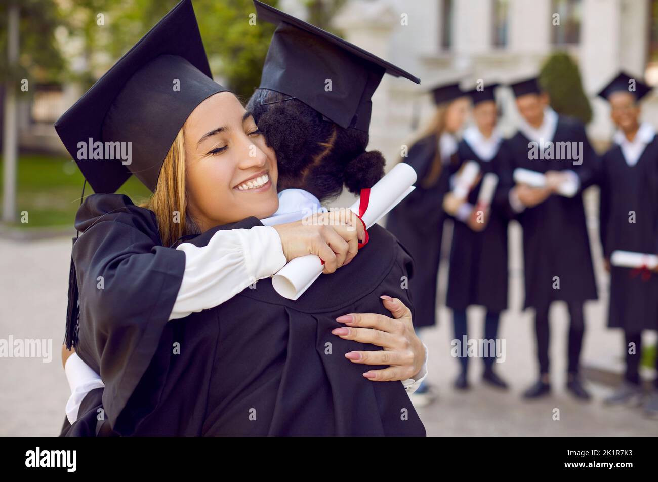 Le donne laureate in abito studentesco si abbracciano dopo essersi laureate all'università o all'università Foto Stock
