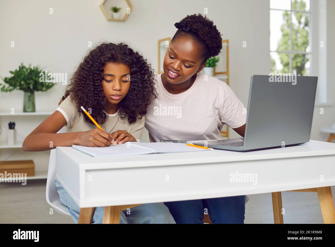 Felice madre afro-americana e bambino piccolo che fa i compiti a casa e utilizzando il PC portatile Foto Stock