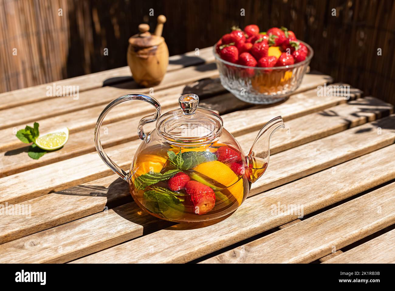 Tè rosso alla frutta con frutti di bosco in una teiera di vetro sul balcone soleggiato. Foto Stock