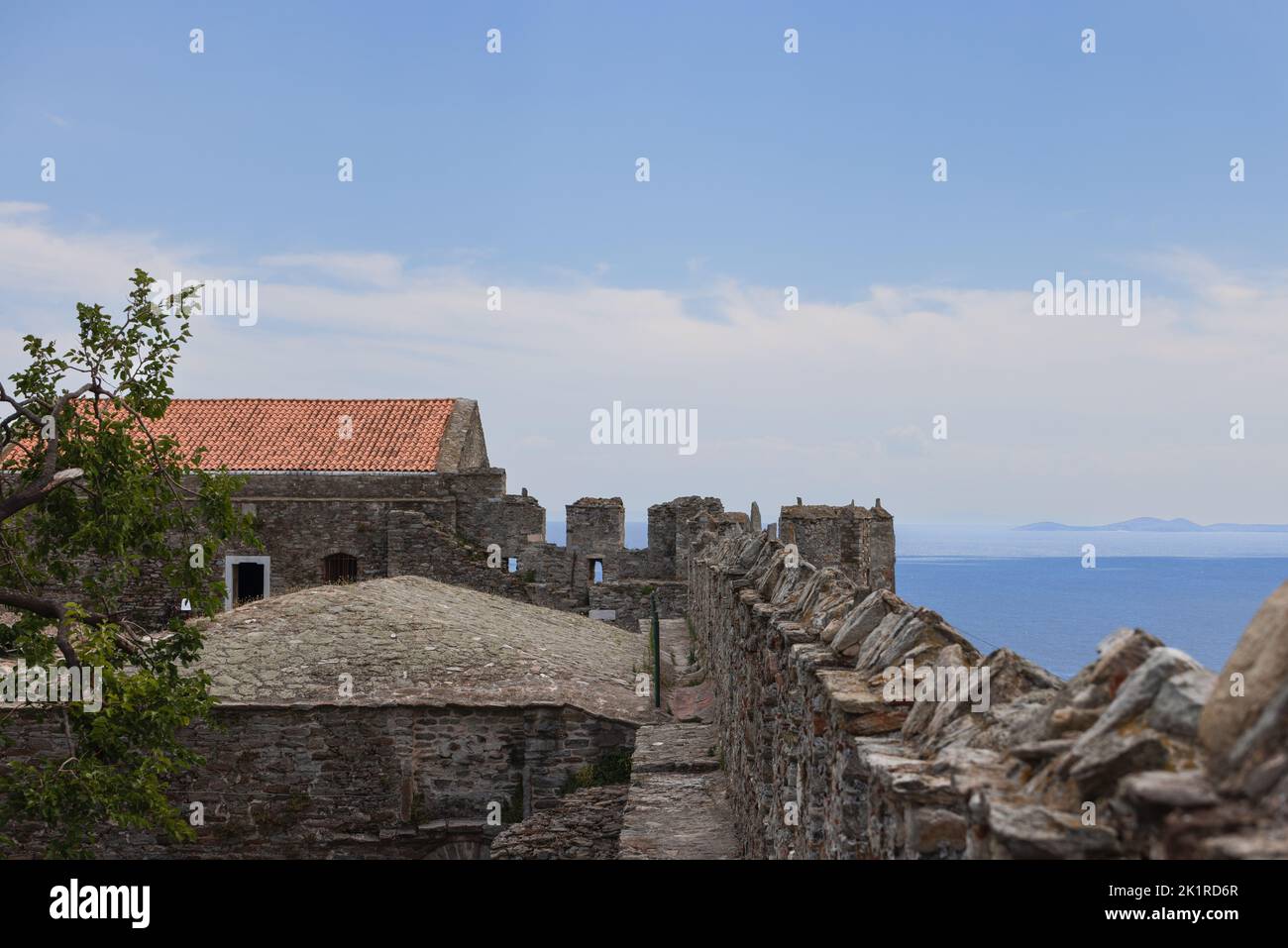 Merlature di mura del castello, orizzonte costituito da mare e catena montuosa silhouette, tetto piastrellato, e albero verde. Kavala, Grecia Foto Stock