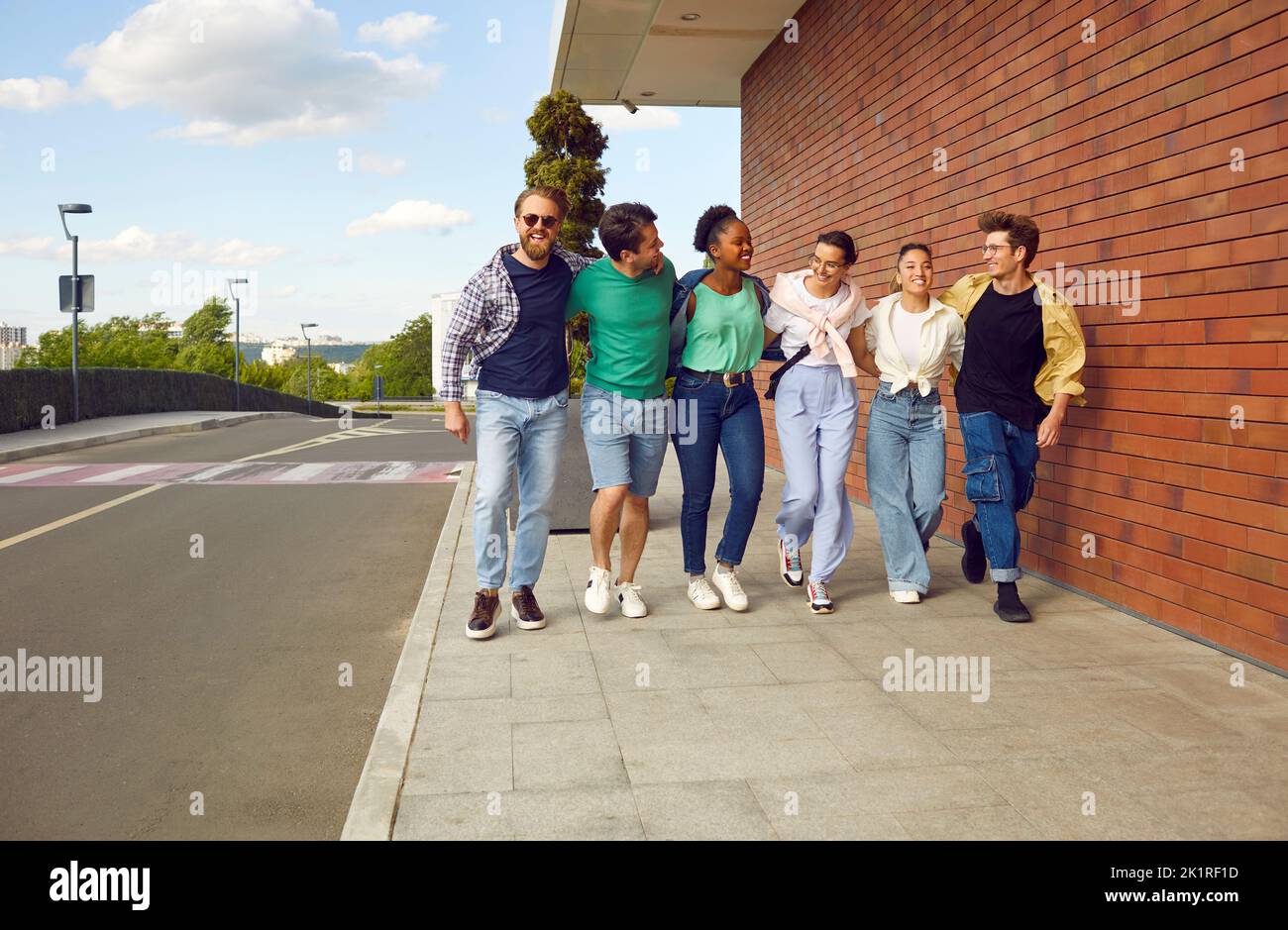 Gruppo di amici allegri e multirazziali camminano insieme per strada in città. Foto Stock