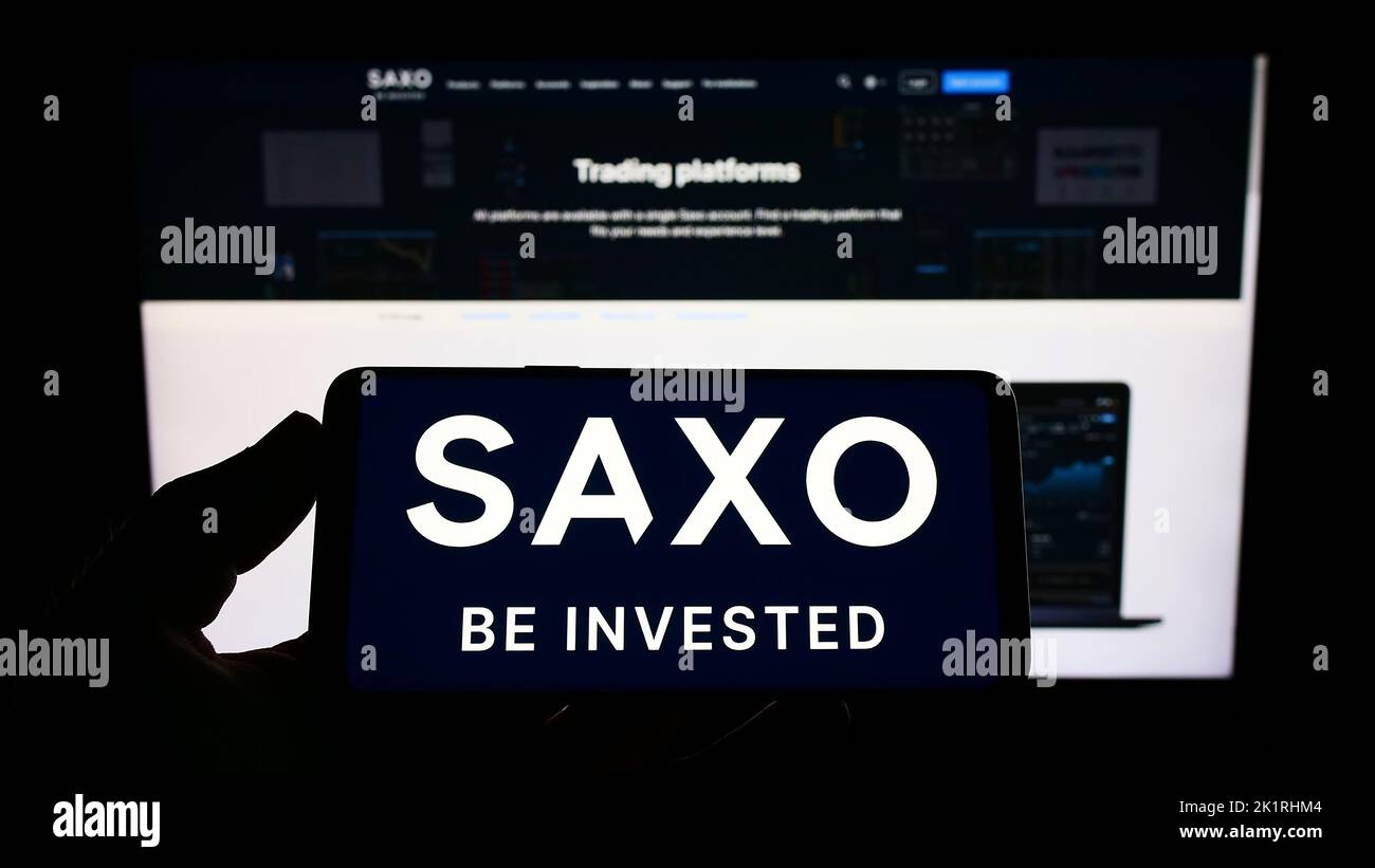 Persona che tiene in mano uno smartphone con il logo della società danese di banche d'investimento Saxo Bank SULLO schermo di fronte al sito Web. Messa a fuoco sul display del telefono. Foto Stock