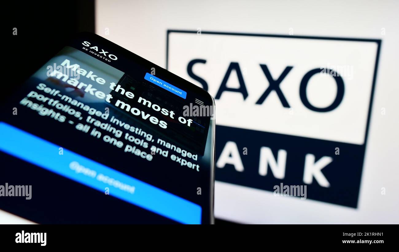 Telefono cellulare con sito web della società danese di banche d'investimento Saxo Bank COME su schermo davanti al logo. Messa a fuoco in alto a sinistra del display del telefono. Foto Stock