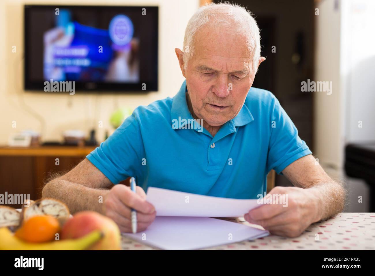 Serio uomo anziano seduto al tavolo scrivendo lettera o riempiendo un certo modulo di carta Foto Stock