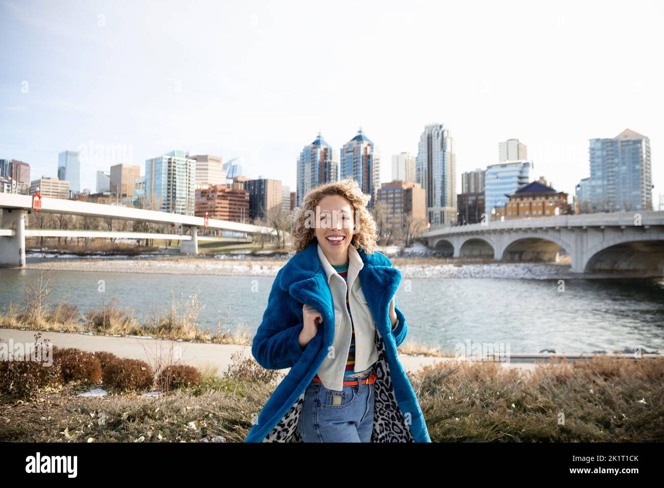Ritratto felice, spensierata giovane donna lungo il fiume città di fronte Foto Stock