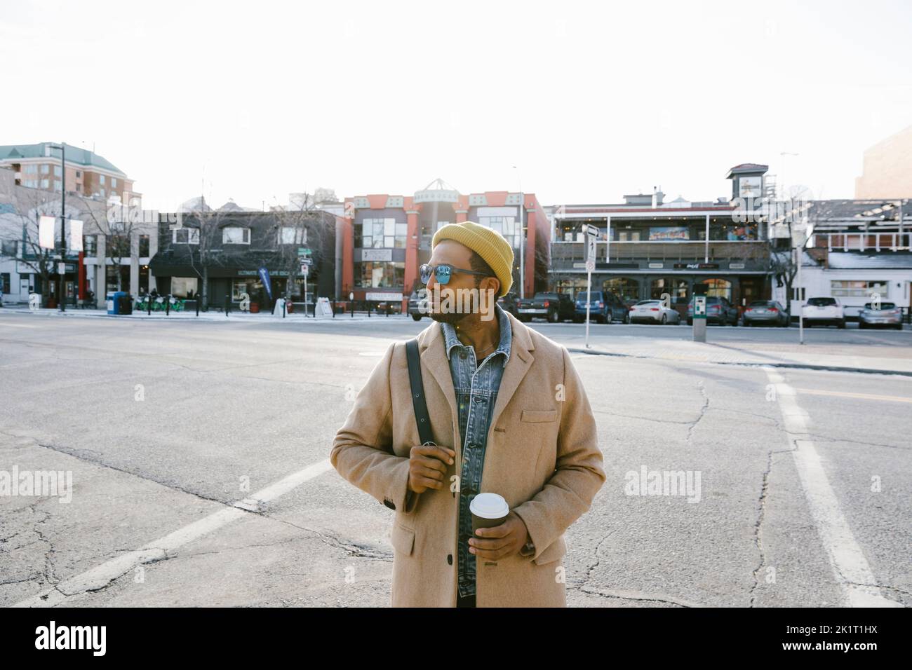 Uomo in occhiali da sole con caffè sulla strada urbana soleggiata Foto Stock