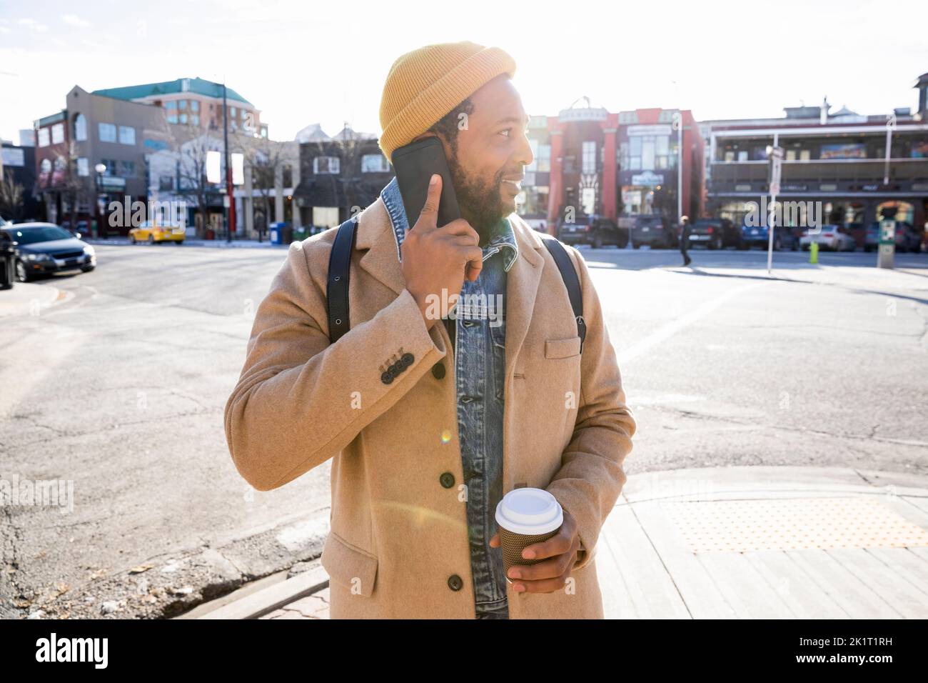 Uomo con caffè che parla sullo smartphone su una strada urbana soleggiata Foto Stock