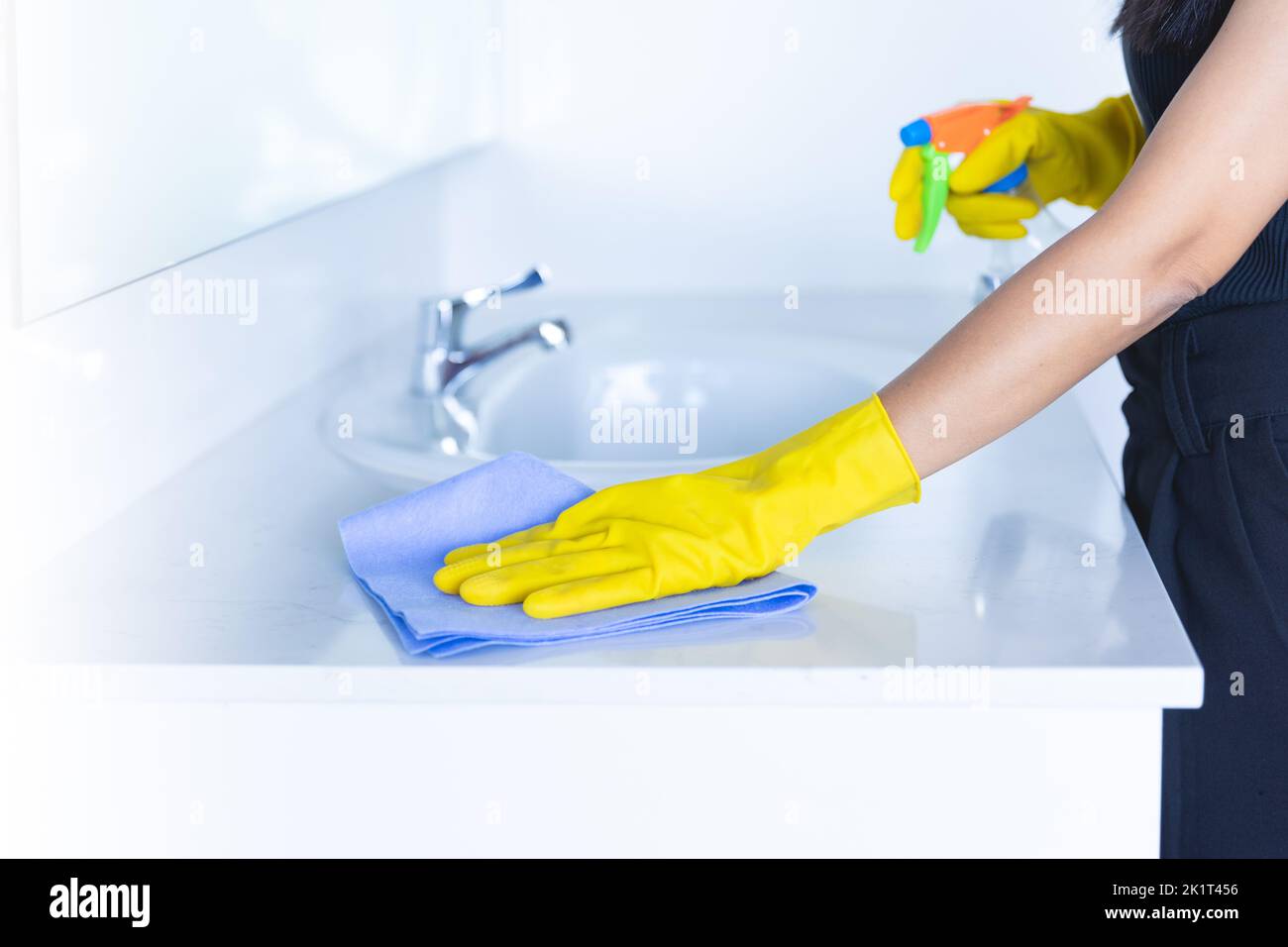 closeup donne lavatrici o charwoman pulizia moderno nuovo lavabo in bagno. Pulire il rubinetto con guanti gialli e un panno blu con disinfettante antinebbia sp Foto Stock