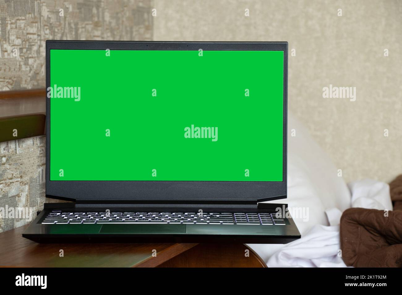 Un computer portatile con uno schermo verde si trova sui comodini vicino al letto dell'appartamento, un computer portatile e il lavoro nel computer Foto Stock