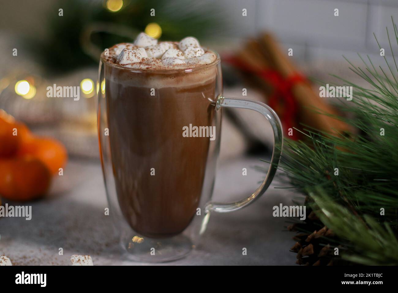 cioccolata calda in una tazza di vetro con mini marshmallows sul tavolo grigio, sfondo di natale sfocato Foto Stock