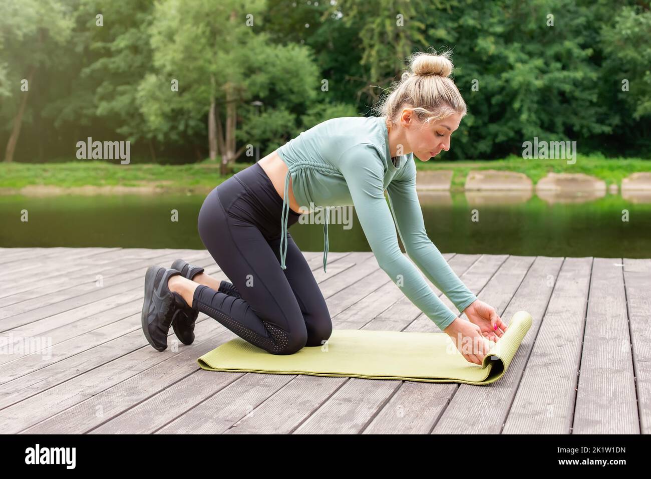 Una donna d'estate in laghetto, svolge un tappetino verde palestra, si prepara per lo sport. Foto Stock