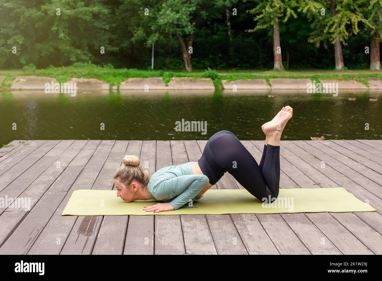 Una donna snella su una piattaforma di legno in estate, fa yoga nel parco Foto Stock