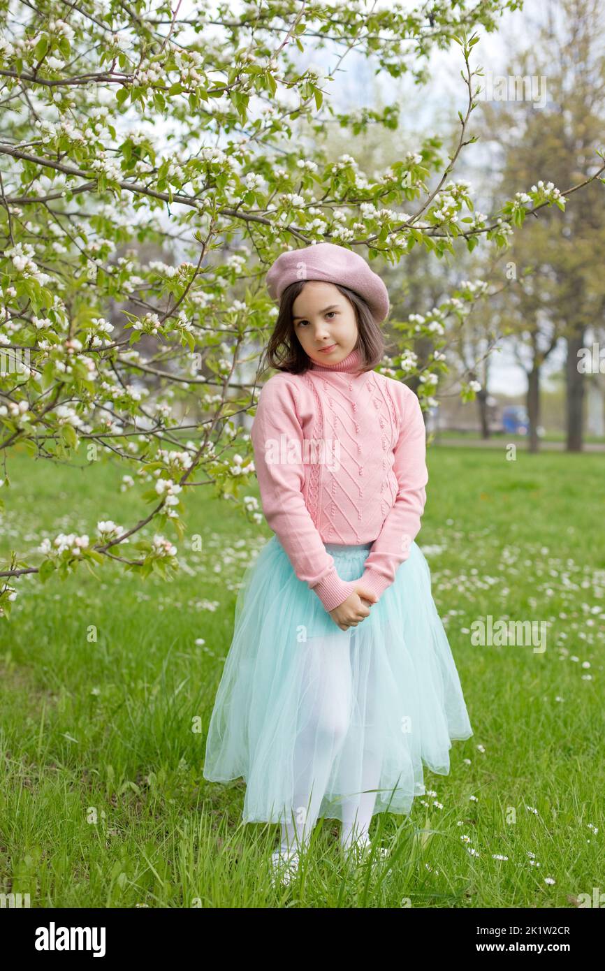 Carina bambina si trova sull'erba verde accanto ad un albero di mela bianco fiorente nel parco. Foto Stock