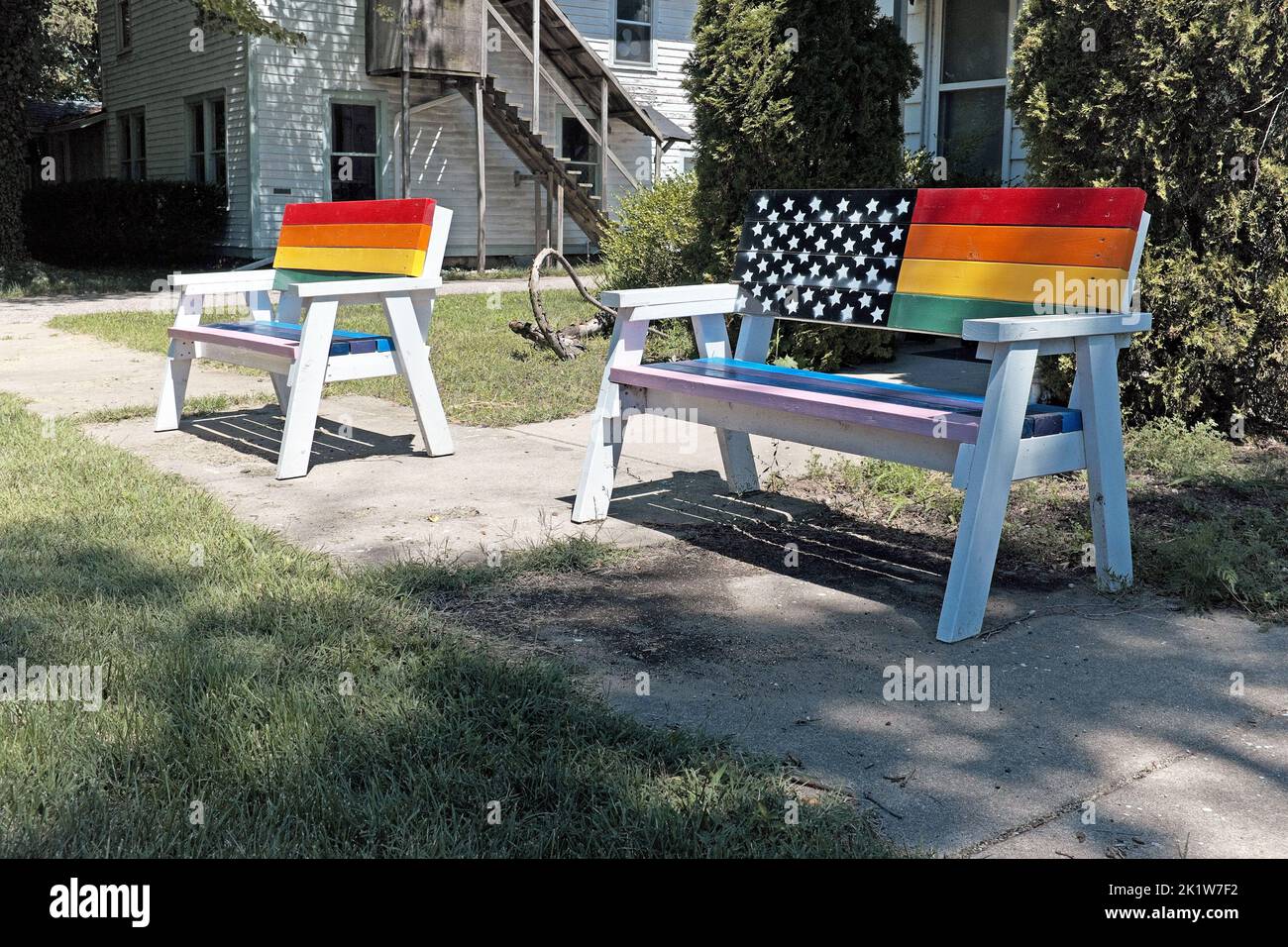 Due panchine dipinte con arcobaleno vuote su un marciapiede pubblico nella comunità pro-LGBTQ di Douglas, Michigan. Foto Stock