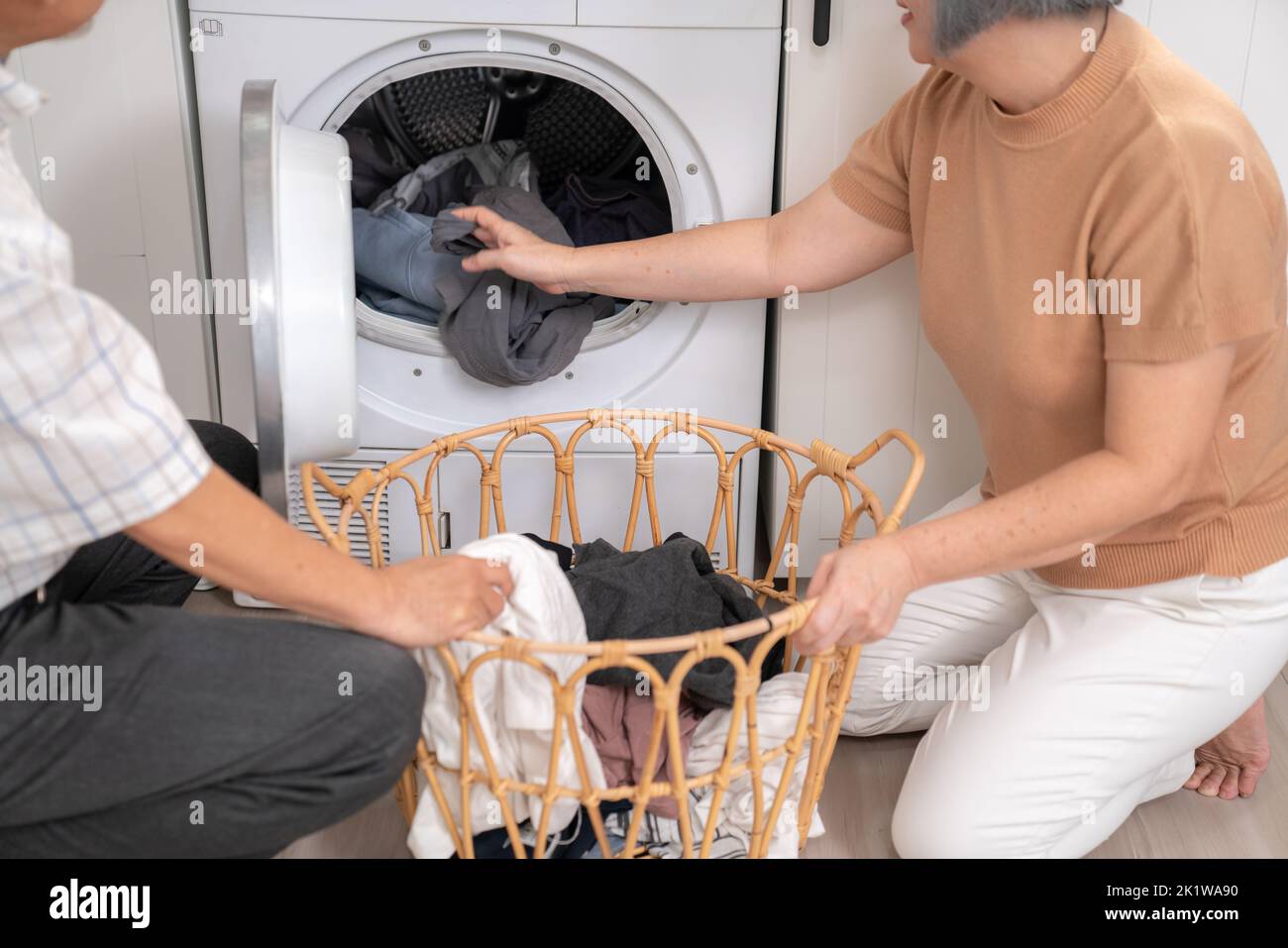 Coppia anziana che lavora insieme per completare le loro faccende domestiche alla lavatrice in un modo felice e soddisfatto. Marito e moglie fanno il Foto Stock