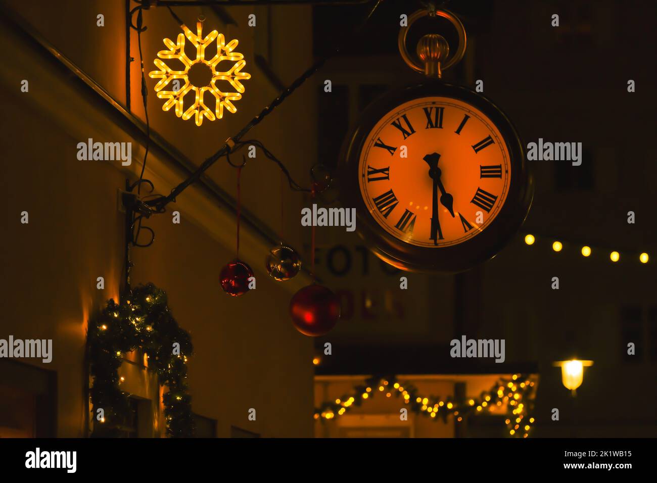 Natale in Europa. Orologio da strada e decorazioni natalizie su sfondo scuro della strada. Atmosfera festosa. Foto Stock