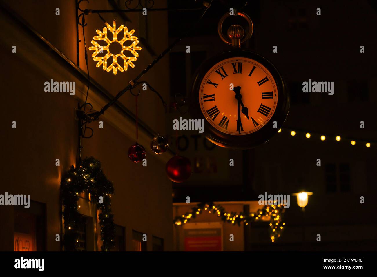 Natale in Europa. Orologio da strada e decorazioni natalizie su sfondo scuro della strada. Foto Stock