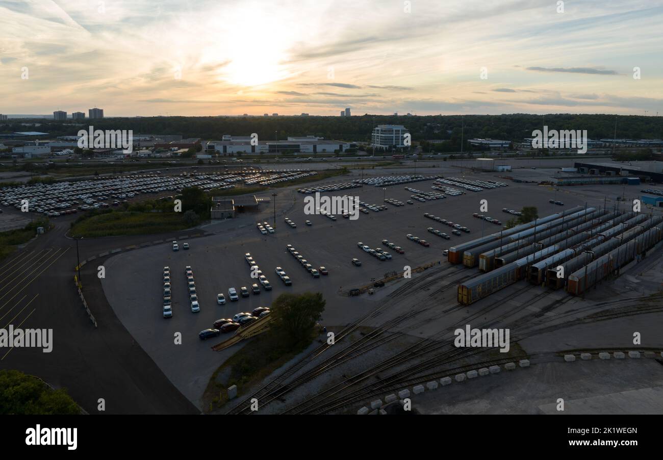 Una vista aerea sopra un parcheggio delle auto Ford di nuova fabbricazione che sono preparate per il trasporto via treno o camion, visto come il sole tramonta. Foto Stock
