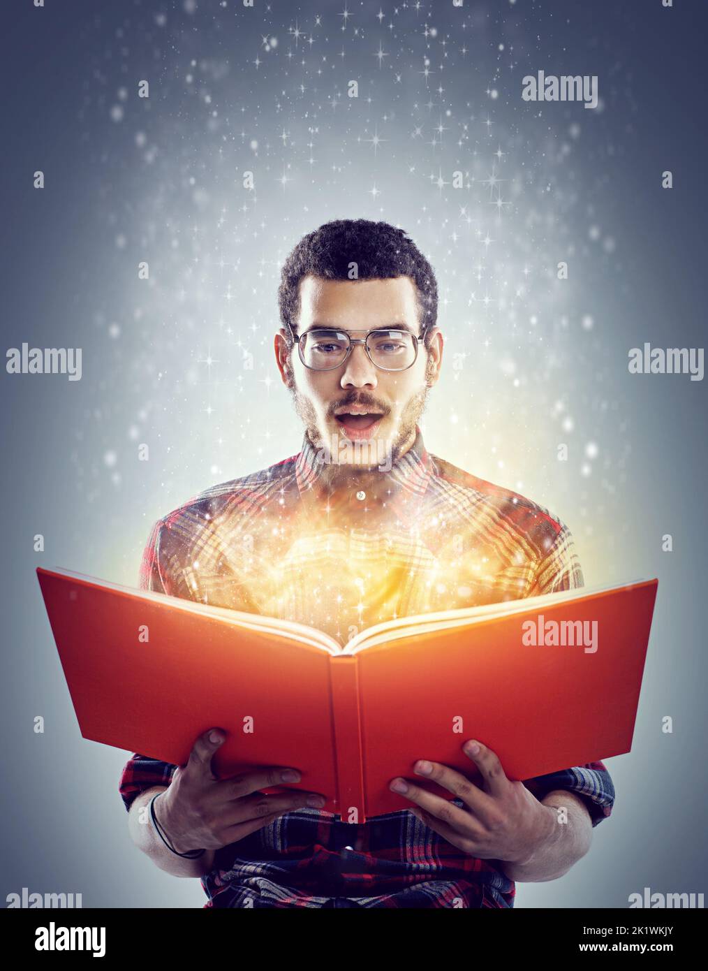 Affascinato dalle sue profondità nascoste. Un'immagine ritagliata di un giovane adulto che legge un libro con pagine incandescenti. Foto Stock