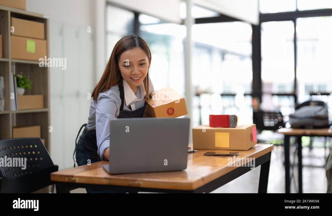 Avvio di piccole imprese. Imprenditore asiatico utilizzando computer portatile controllare l'ordine online e prepararsi a imballaggio per il cliente. Business PMI di successo Foto Stock