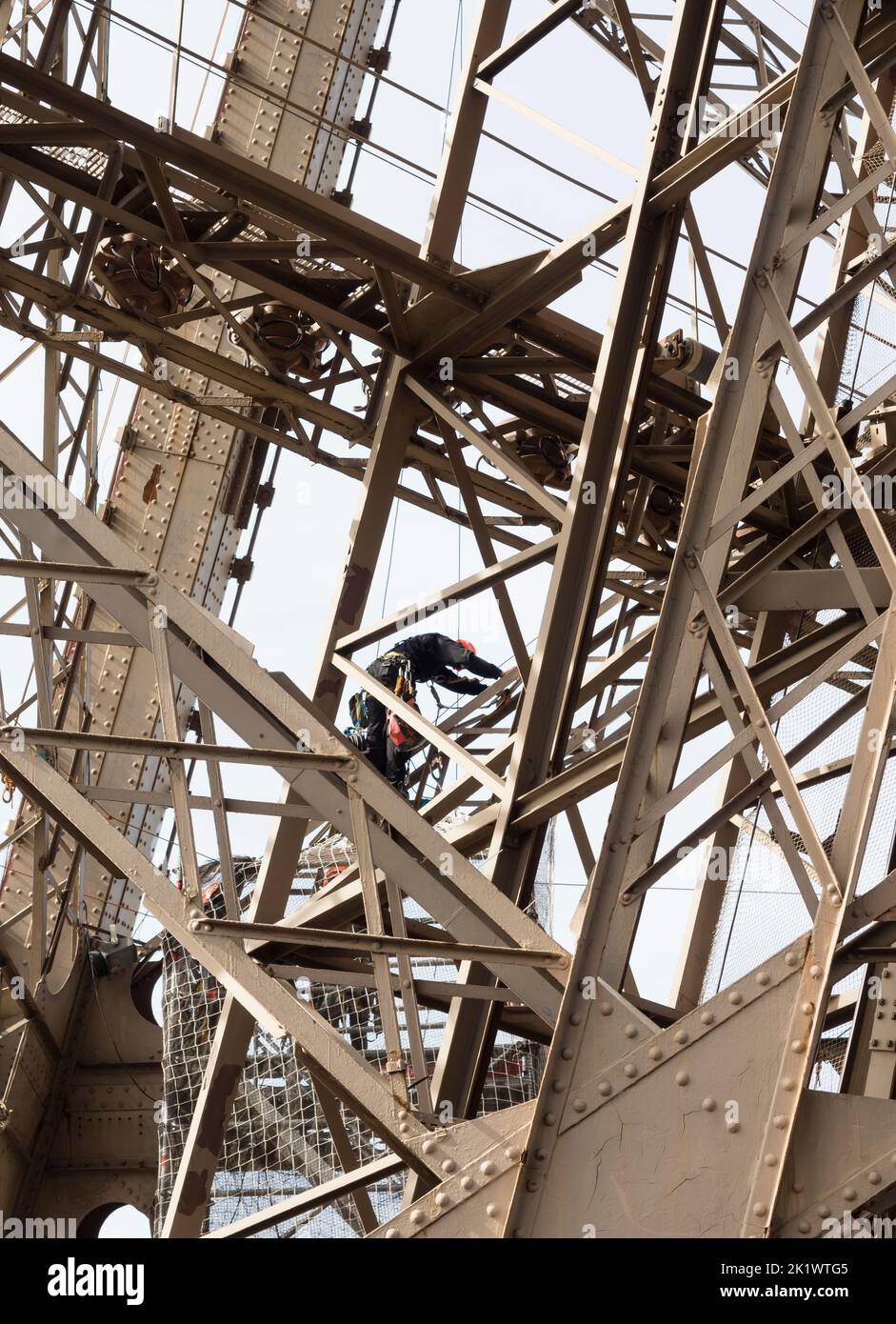 Un pittore su una corda sta scalando la struttura in acciaio della Torre Eiffel di Parigi. Foto Stock