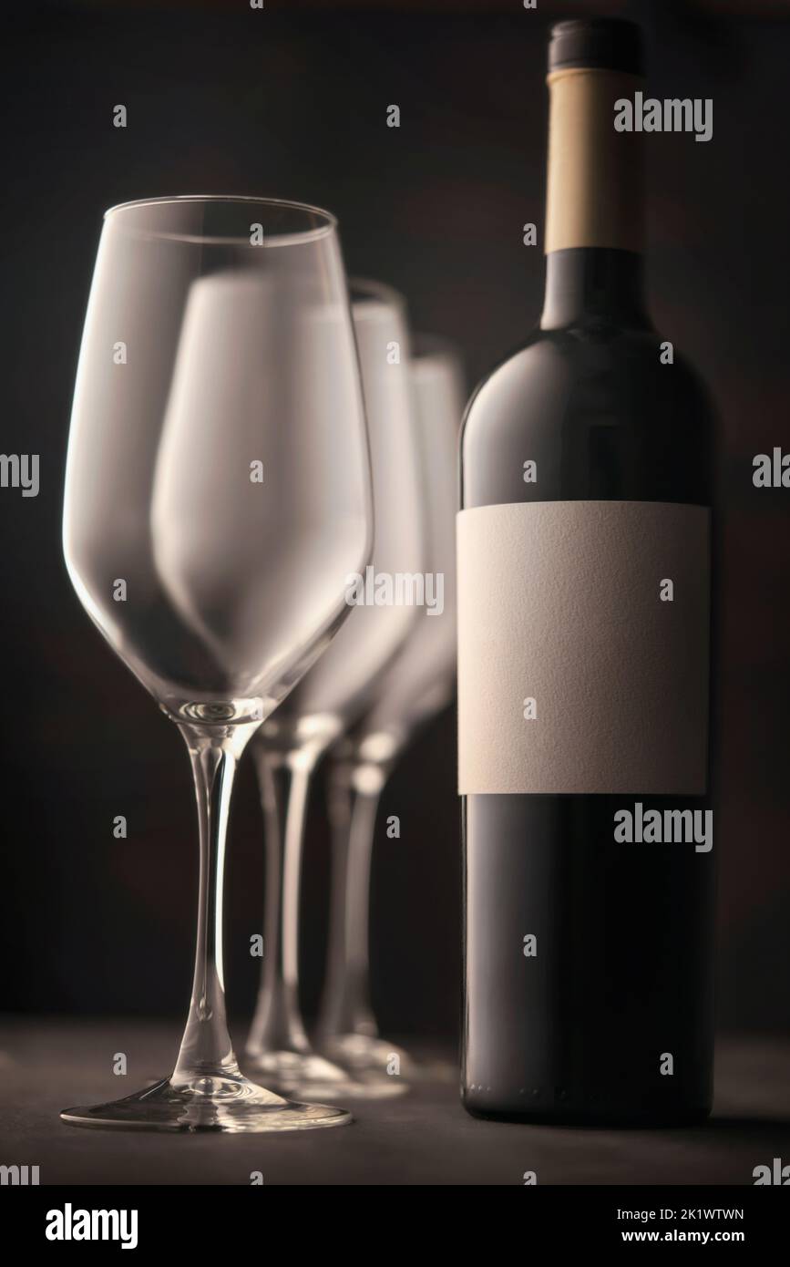 bicchieri da vino e una bottiglia di vino rosso con etichetta bianca senza iscrizione. Bella vita soulful, sfondo scuro atmosfera atmosfera. Foto Stock