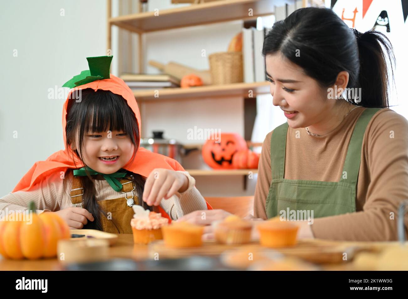 Felice concetto di famiglia. Giocoso e cute giovane ragazza asiatica in costume di Halloween ama fare un cupcake di Halloween con la sua mamma. Foto Stock