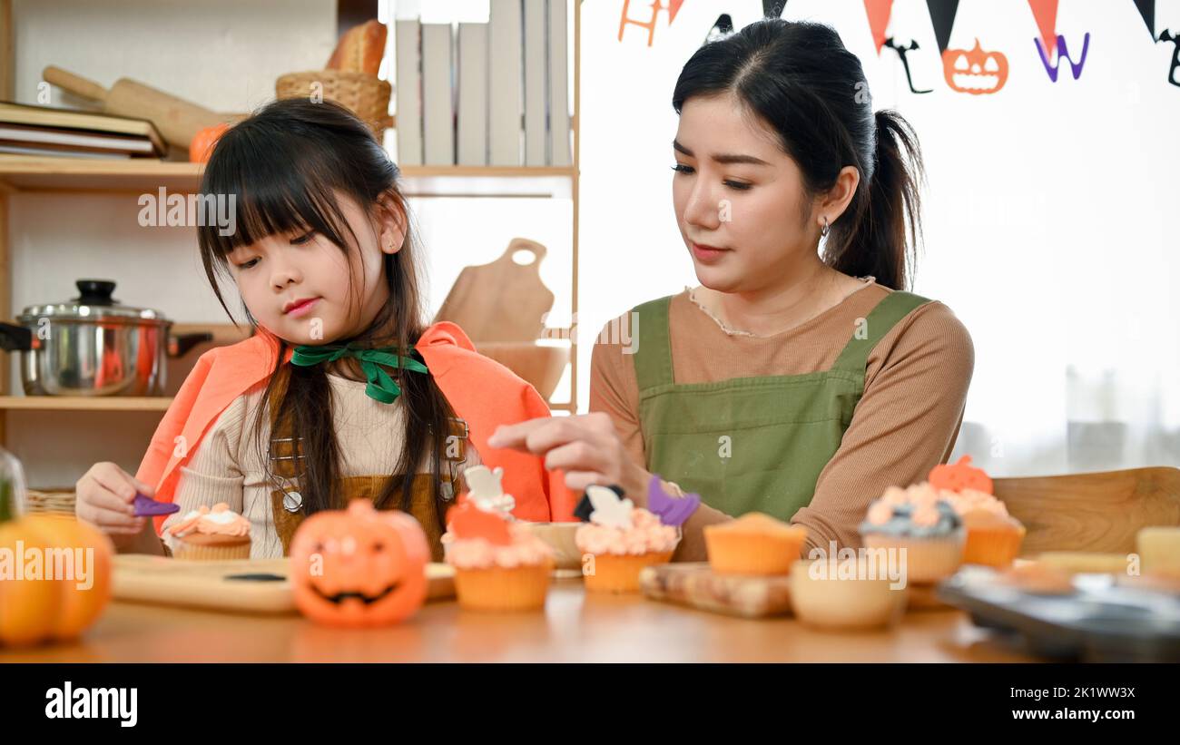 Ragazza asiatica cute che decorano il suo cupcake di Halloween con la sua mamma in cucina. Concetto di attività della famiglia di Halloween Foto Stock