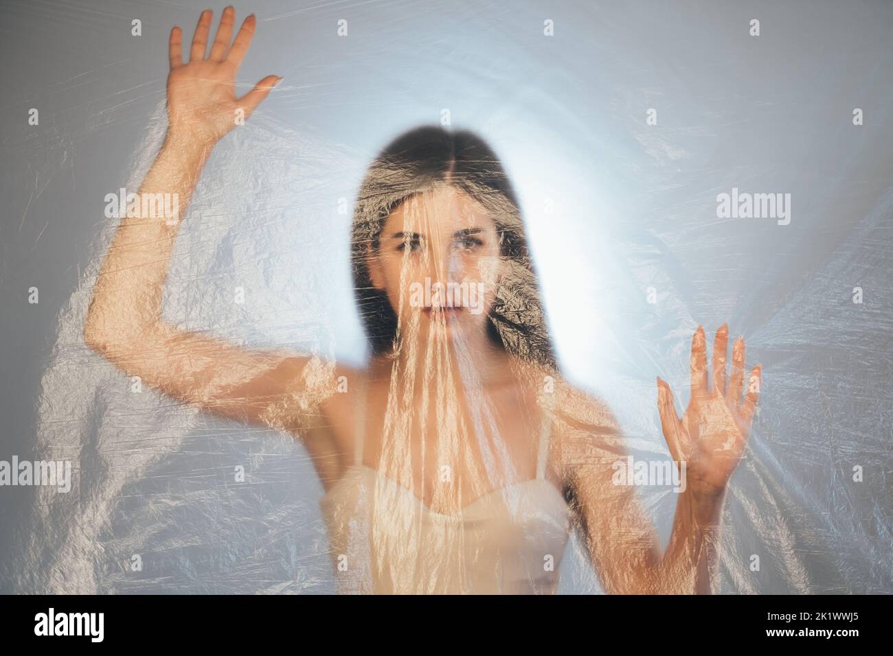Protezione femminile. Ritratto sfocato. Discriminazione di genere. Disturbato preoccupato donna intrappolata dietro trasparente rugoso pellicola di polietilene tex Foto Stock