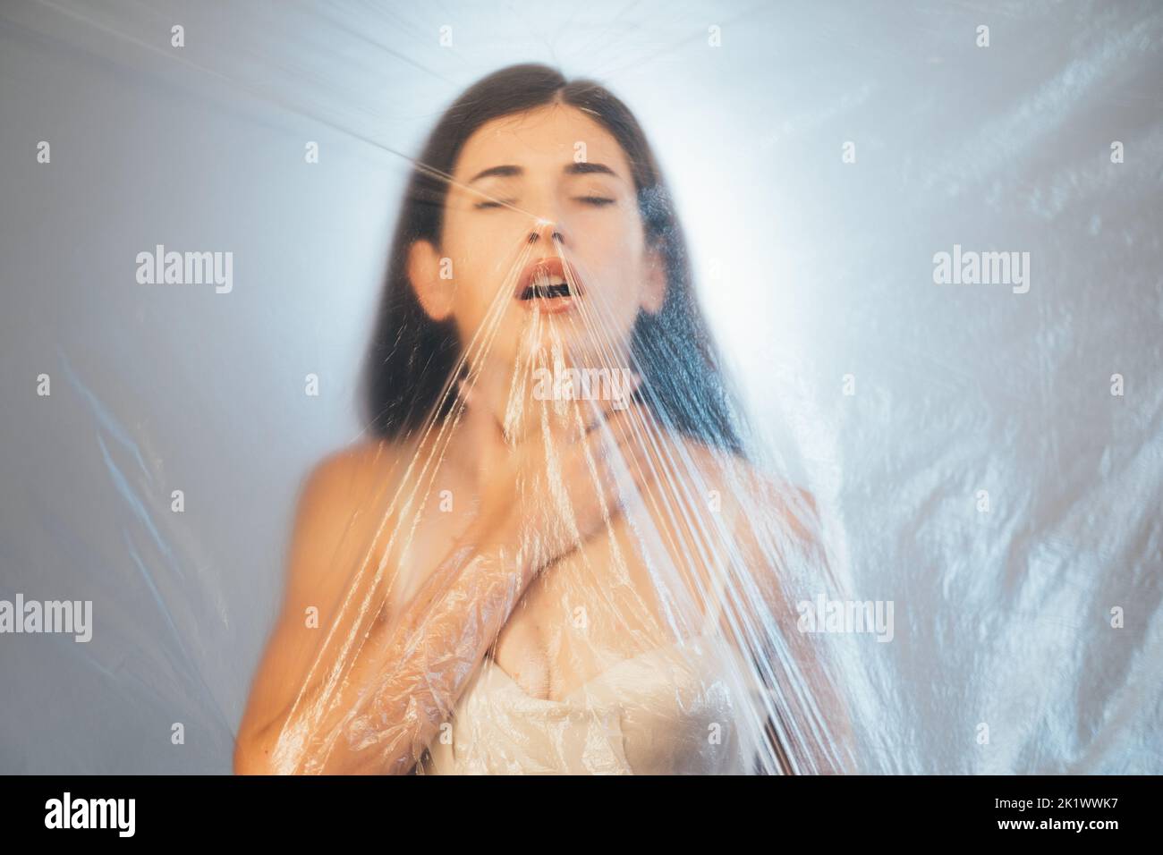Respiro corto. Ritratto sfocato. Inquinamento atmosferico. Allergia asma. Donna sofferente con gola che tocca la gola dietro la polietia grinzita trasparente Foto Stock