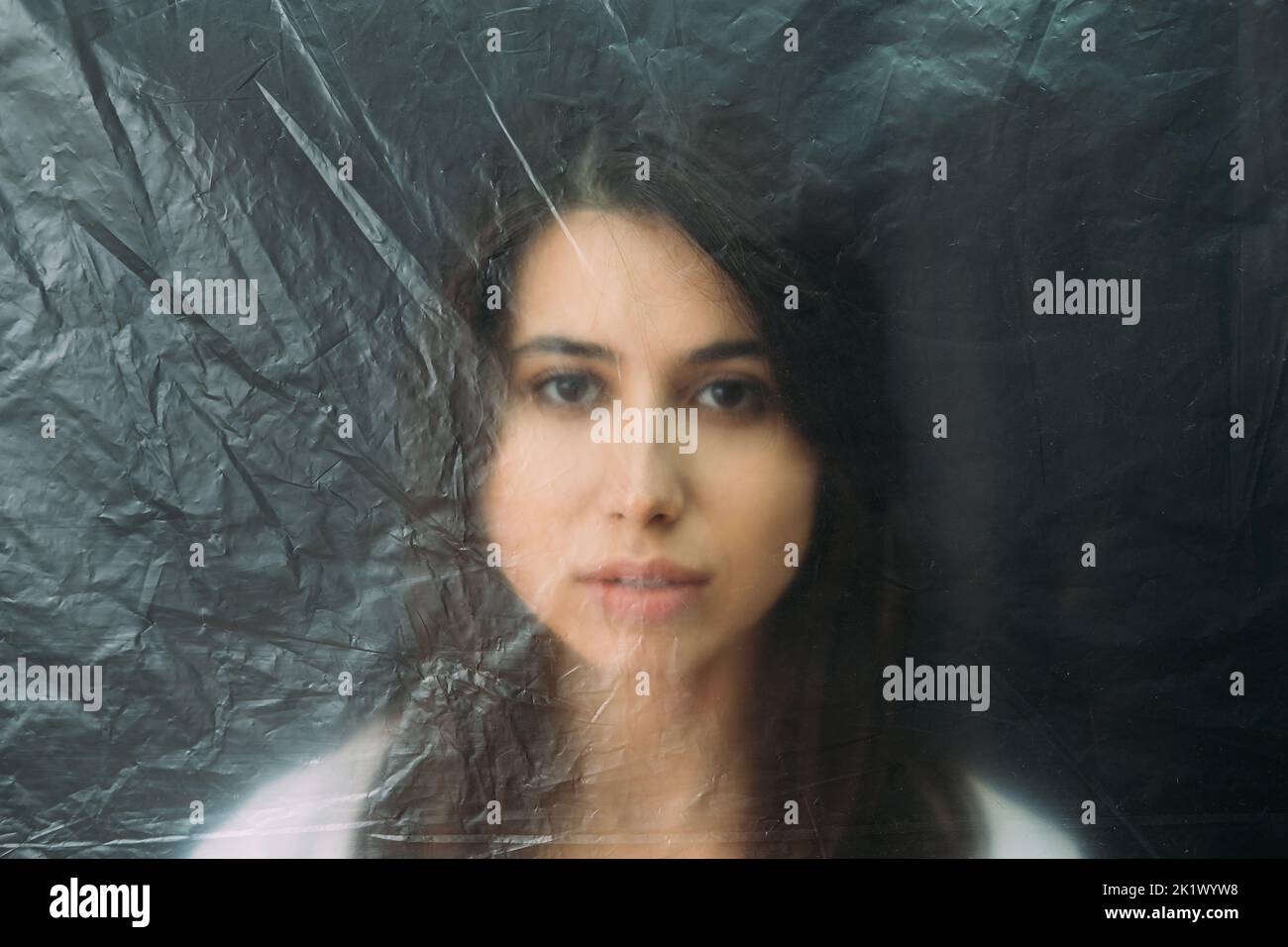 Diritti delle donne. Ritratto sfocato. Isolamento sociale. Discriminazione solitudine. Donna vulnerabile faccia dietro tessuto grinzito polietilene trasparente Foto Stock