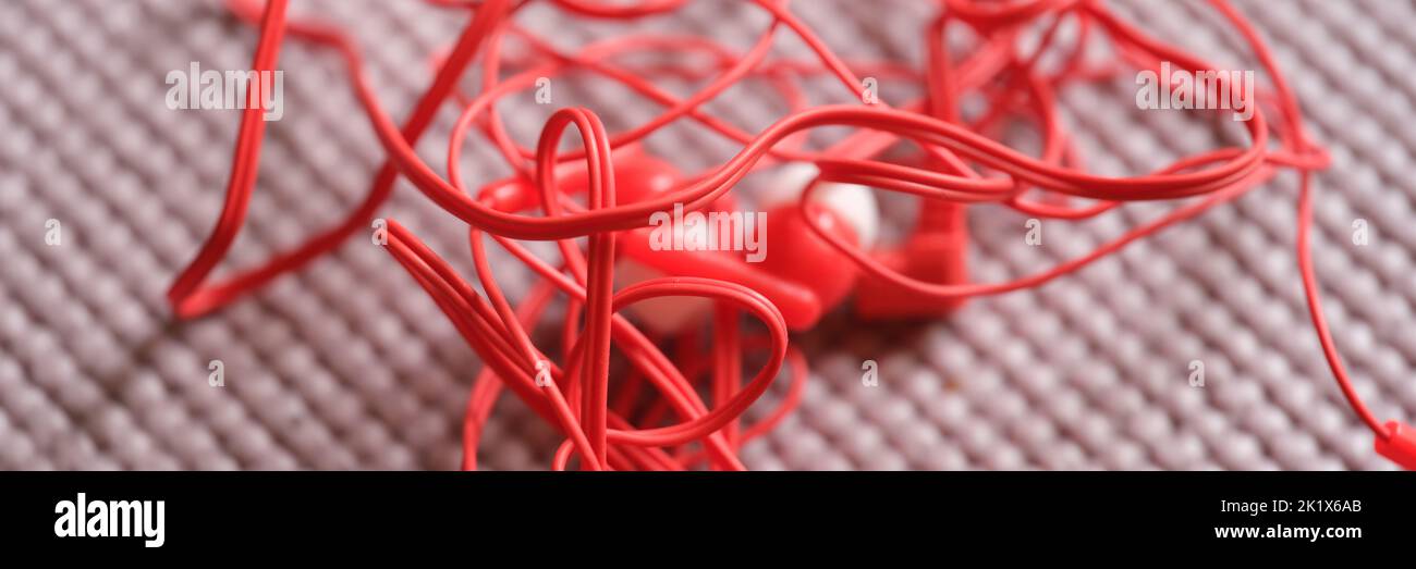Cuffie con filo rosso aggrovigliate su sfondo grigio Foto Stock