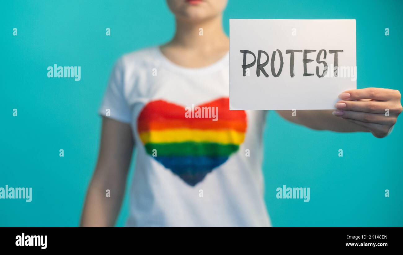 Protesta per i diritti delle donne. Dimostrazione sociale. Parità di genere. Emancipazione femminile. Ragazza defocusa con segno contro la discriminazione in t-shirt con arcobaleno Foto Stock