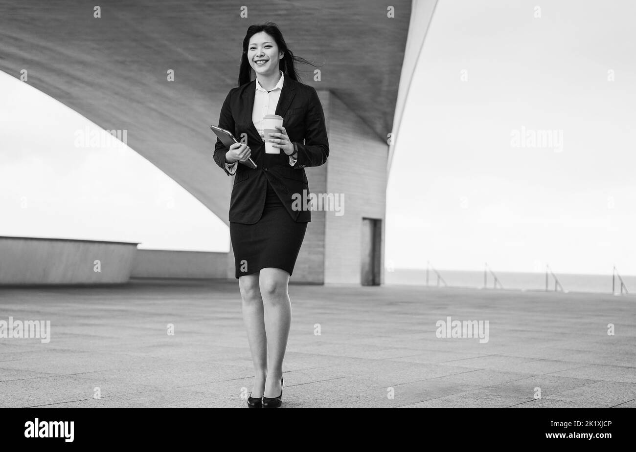 Donna asiatica d'affari che cammina per lavorare all'aperto - Focus on Face - montaggio in bianco e nero Foto Stock