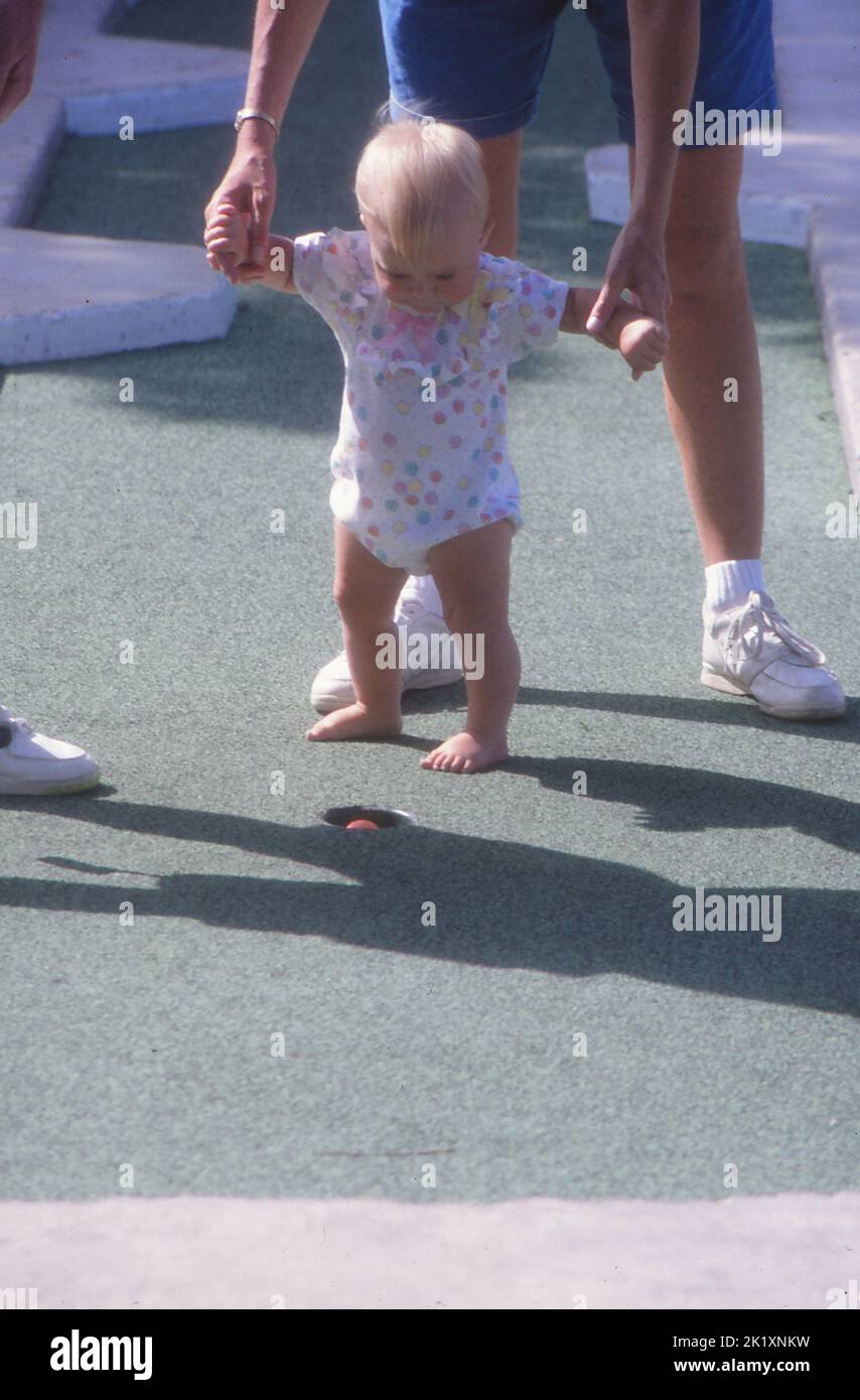 Un colpo verticale di un genitore che tiene un bambino mentre la sfera del croquet cade nel foro Foto Stock