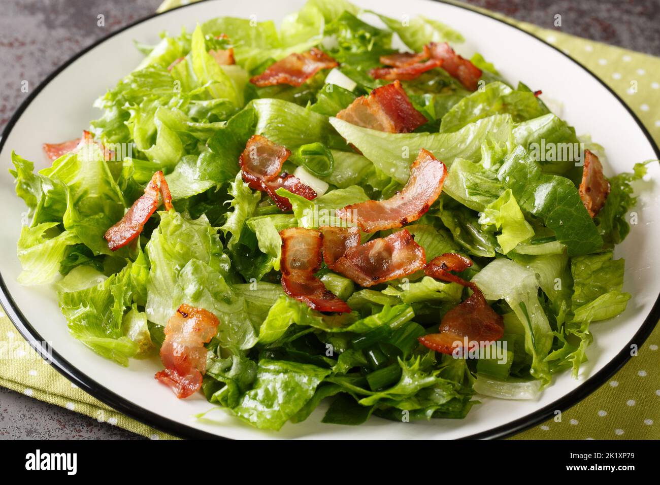 Insalata americana di lattuga appassita con strisce di pancetta primo piano nel piatto sul tavolo. Orizzontale Foto Stock
