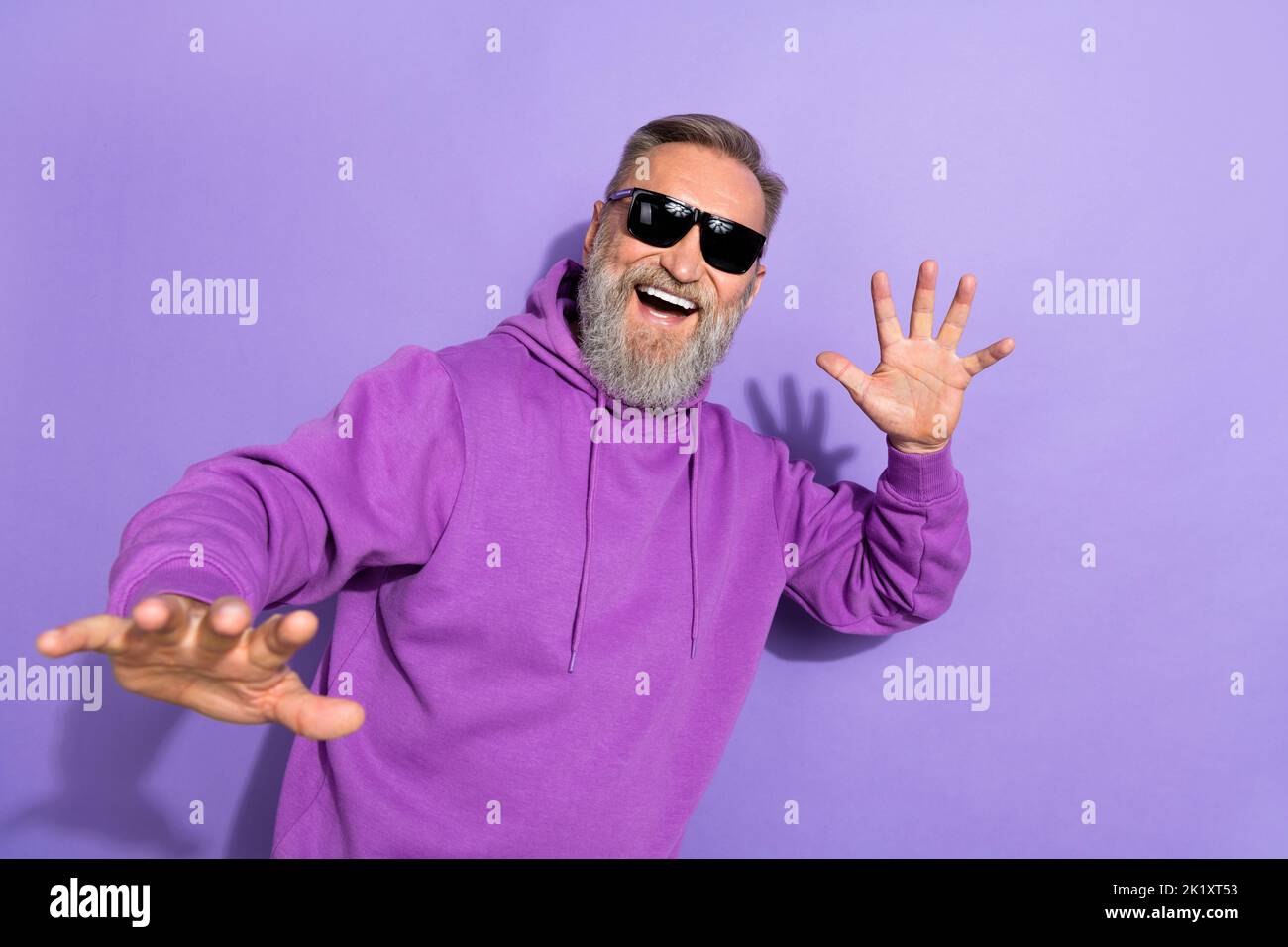 Foto di bel vecchio uomo spensierato con barba bianca grigia indossare felpa viola dimostrare mano isolata su sfondo di colore viola Foto Stock