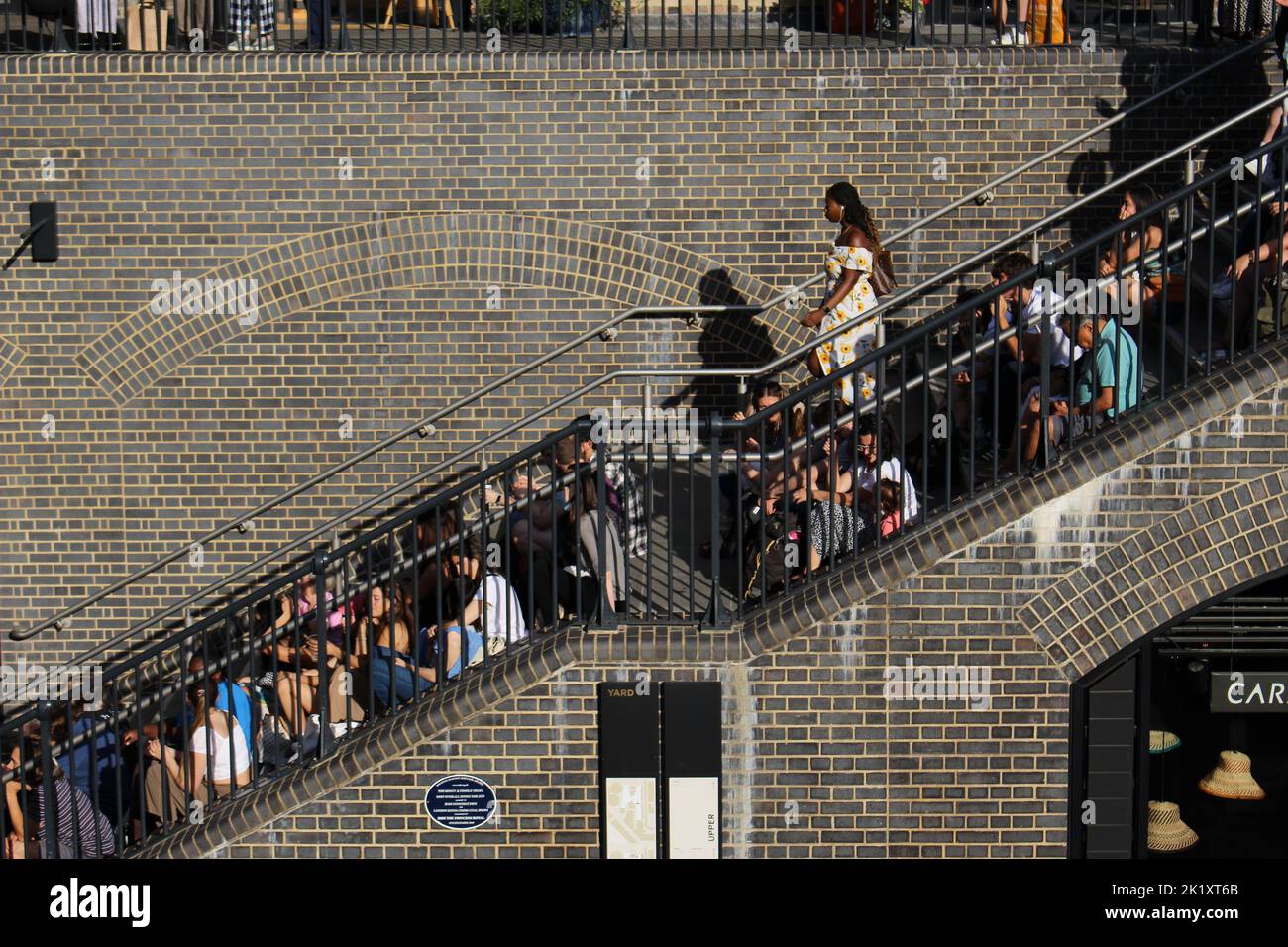 La gente gode di un concerto gratuito del festival dei suoni estivi di Kings Cross al Coal Drops Yard. Il posto era così pieno di persone che si sedettevano sulle scale Foto Stock