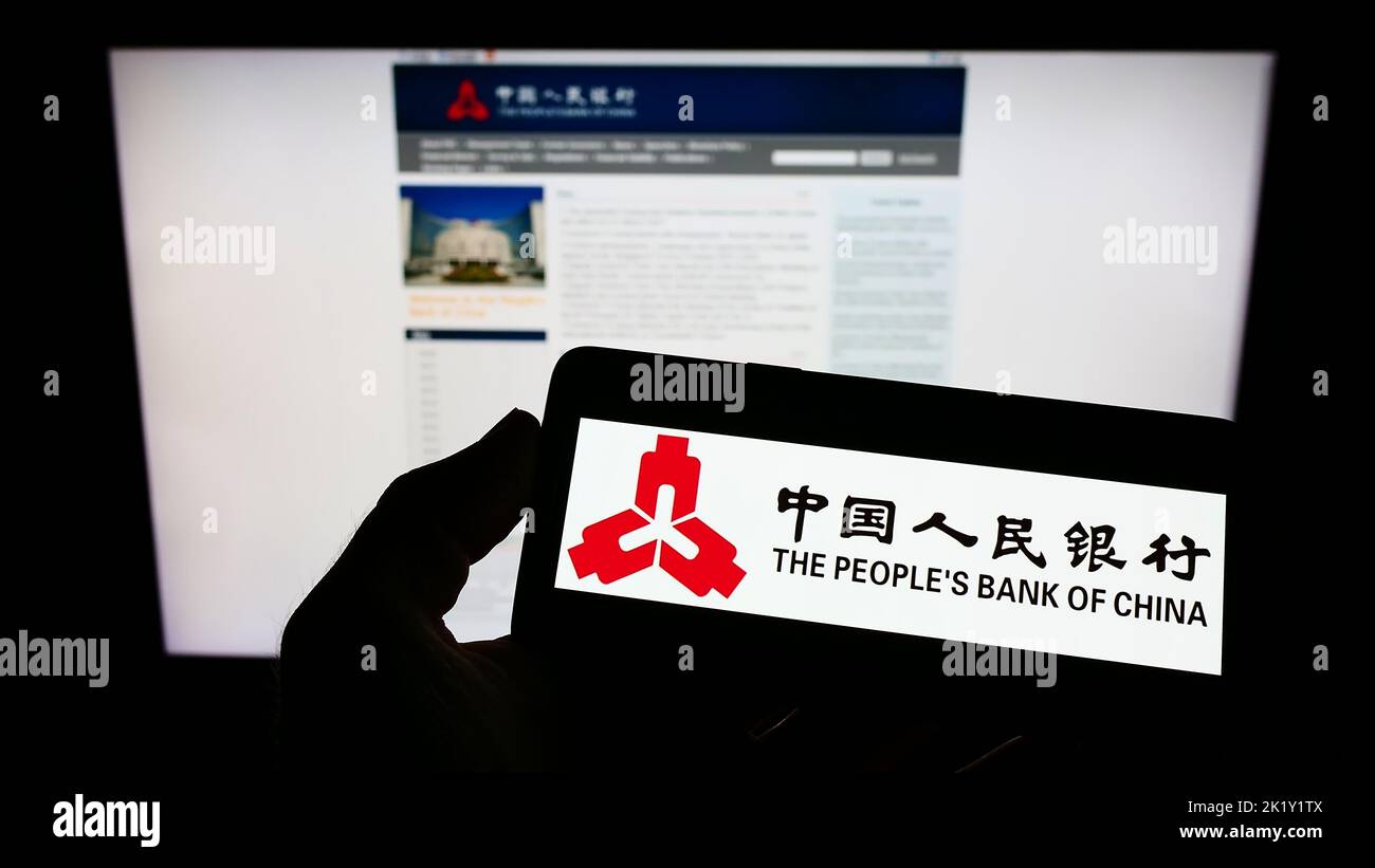 Persona che tiene in mano uno smartphone con il logo della People's Bank of China dell'istituto finanziario sullo schermo di fronte al sito Web. Messa a fuoco sul display del telefono. Foto Stock