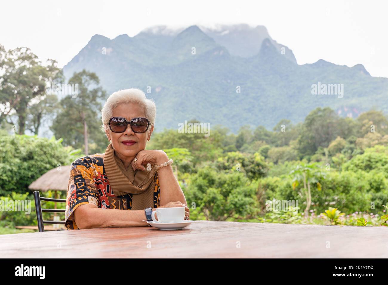 ASIN grigio capelli bianchi donna anziana bere caffè in caffè all'aperto con vista sulle montagne. Foto Stock